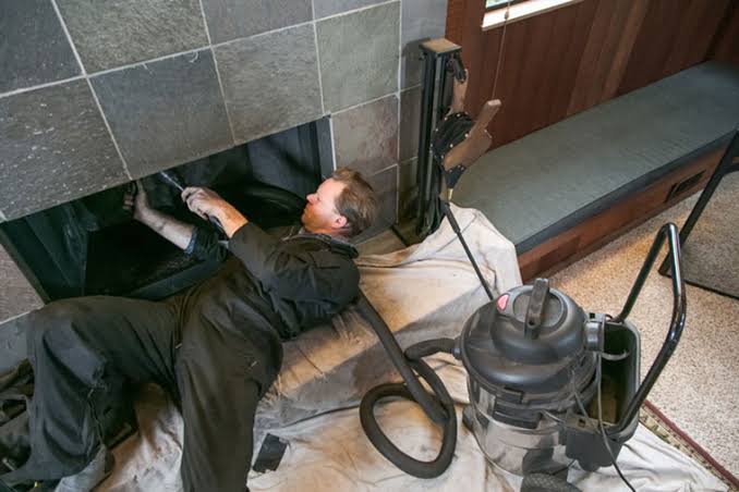 Person cleaning the inside of a tiled fireplace with a vacuum and protective drop cloth